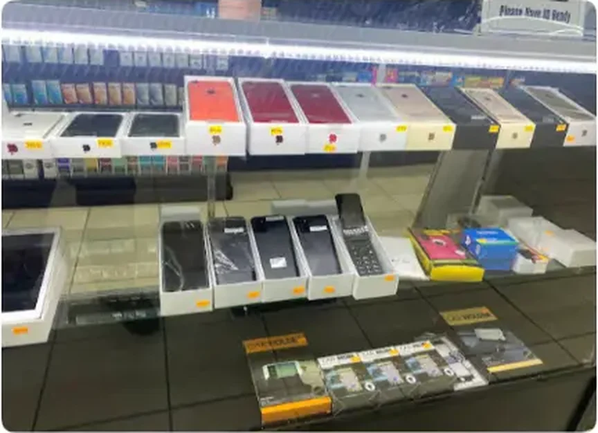 Mega Tobacco Vape & Wireless row of boxed phones, cases and accessories laid out along the lit wireless counter